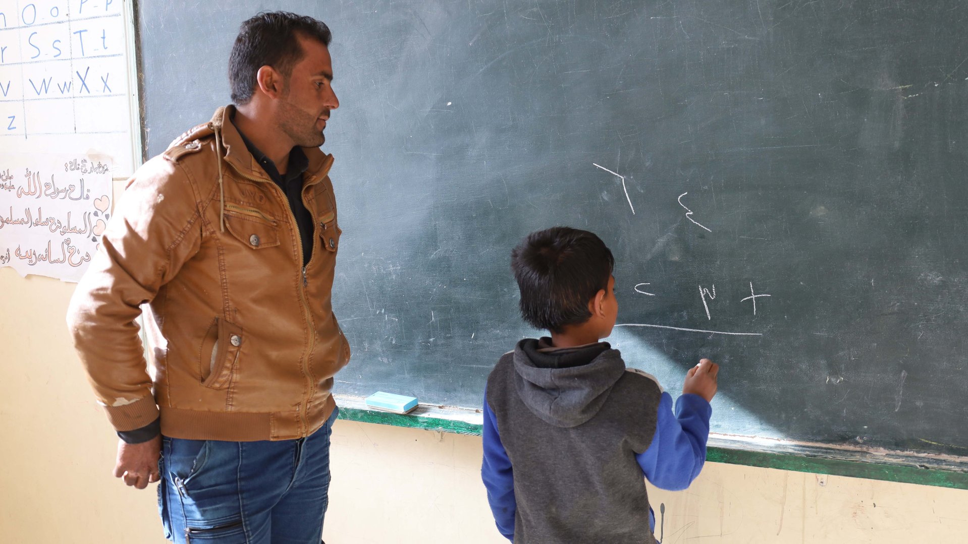 Muhammad, 9 years old, with his teacher at the chalkboard, as part of War Child's Syria Response